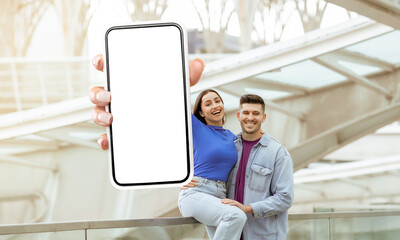 Poster - A man and woman are standing together, holding up a cell phone with white blank screen, mockup copy space. Traveling app