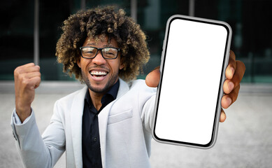 Poster - African American man dressed in a suit standing while holding up a cell phone, looking at the screen intently. He appears focused and engaged in whatever is displayed on the device.