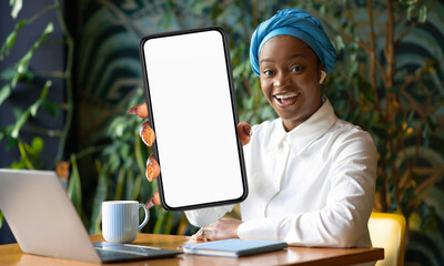 Poster - African American woman is seated at a table, engaged with a laptop computer. She appears focused on the screen, possibly working or studying, showing phone with white screen