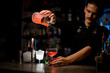Bartender holds a cocktail glass high and pours the drink into a stemmed glass