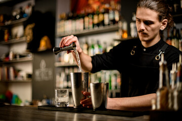 Bartender pours clear cocktail liquid from jigger into shaker and will prepare cocktail