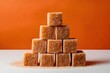 Stack of brown sugar cubes forming pyramid, top cube protruding, against white background