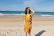Woman in yellow dress standing on beach with ocean in background on sunny day with clear blue sky