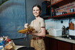 Happy woman holding gold gift box in kitchen, smiling brightly, expressing gratitude and joy