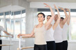 Group of men and women practicing third ballet position at barre in dance studio