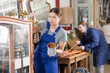 Skilled female furniture repair specialist in uniform restoring and painting furniture during workday in workshop
