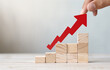 A hand is pointing at a red arrow on top of a stack of wooden blocks. Concept of progress and growth, as the arrow represents a positive upward trend