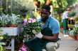 African American man florist arranging ornamental plants in pots while gardening in glasshouse