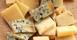 Large pile of traditional hard and blue cheese selection on wooden board