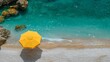 A serene bird's eye view of a yellow umbrella on a sandy beach next to crystal clear turquoise waters, capturing a moment of tranquil solitude