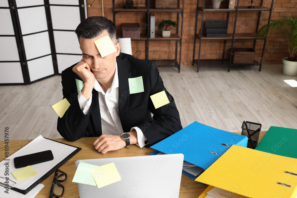 Stressed businessman with sticky notes working under deadline in office
