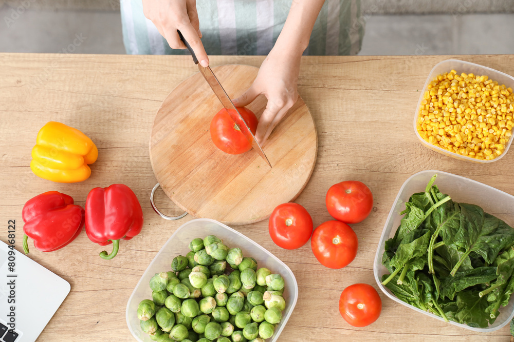 Woman cutting fresh tomatoes for freezing on wooden table