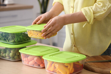 Wall Mural - Woman putting plastic containers with vegetables for freezing on table, closeup
