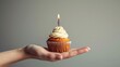   A hand holds a cupcake with a single candle inserted in it