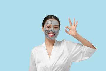 Wall Mural - Young woman with clay mask on her face showing OK against blue background