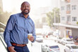 © peopleimages.com - Black man, portrait and office balcony in city with drink, summer and corporate employee for work break. Male entrepreneur, coffee and railing in workplace with smile, business career and sunshine