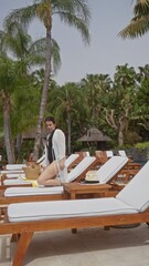 Wall Mural - A relaxed woman enjoys a sunny day at a tropical bali resort, surrounded by palm trees and loungers.