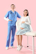 © Pixel-Shot - Young pregnant woman sitting on couch with doctor against pink background