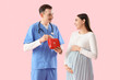 © Pixel-Shot - Young pregnant woman and doctor with first aid kit on pink background