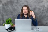 Fototapeta Tęcza - Young man with long hair in blue suit posing in front of laptop and accessories