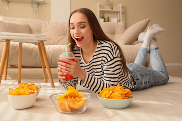 Wall Mural - Young woman with soda and bowls of chips lying on floor at home