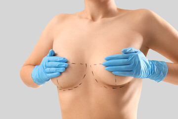 Poster - Naked young woman in medical gloves with marks on her breasts against light background, closeup. Plastic surgery concept