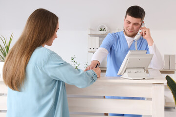 Canvas Print - Male receptionist with patient talking by phone at desk in clinic