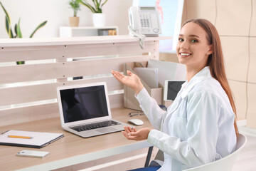 Canvas Print - Female receptionist sitting at desk in clinic