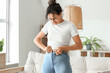 © Pixel-Shot - Young African-American woman trying to button tight pants at home. Diet concept