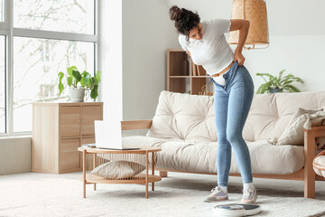 Canvas Print - Young African-American woman trying to put on tight pants at home. Diet concept