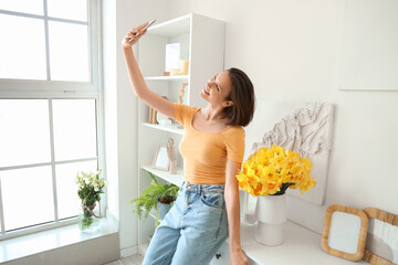 Poster - Young woman taking selfie with daffodils in vase on commode at home