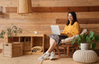 © Pixel-Shot - Young woman using laptop in armchair near wooden wall at home