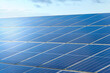 Blue solar cells in a solar panels power farm or photovoltaic cell park reflecting the blue cloudy sky and sun. Green Energy Concept. Image with copy space