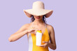© Pixel-Shot - Beautiful young African-American woman in swimsuit and wicker hat with bottle of sunscreen cream on lilac background