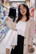 A smiling Asian woman stands in a grocery aisle, holding shopping bags, shopping in a supermarket.