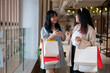 Two Asian women stand together in a shopping mall corridor, looking at a smartphone.