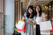 Two joyful Asian women holding shopping bags in a shopping mall, having a fun shopping day together.