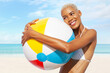 Smiling girl at the beach side holds inflatable beach ball, wearing bikini feels great, African latin American woman. Concept of a seaside holiday or shopping for a summer beach holiday