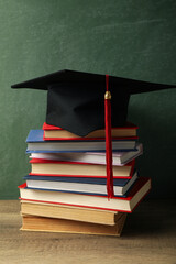 Wall Mural - Graduation hat with books on a table on a dark background.