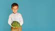 A studio shot of a boy holding fresh broccoli on a blue background with a copy of the space. The concept of healthy baby food.
