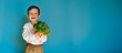 A studio shot of a smiling boy holding fresh broccoli on a blue background with a copy of the space. The concept of healthy baby food.