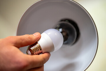 white led light bulb in male`s hand, holding it near the the lamp with incandescent bulb. changing t