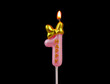 Burning pink birthday candle with golden bow isolated on black background, number 1.	