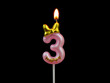 Burning pink birthday candle with golden bow isolated on black background, number 3.	