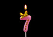 Burning pink birthday candle with golden bow isolated on black background, number 7.	