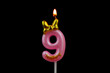 Burning pink birthday candle with golden bow isolated on black background, number 9.	