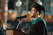 Valedictorian young student man giving graduation speech to other graduated people
