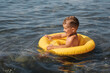 Cute baby boy swims in a yellow inflatable circle in the sea on the beach.