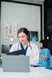 © Nuttapong punna - Young female doctor in white medical uniform using laptop and tablet talking video conference call at desk,Doctor sitting at desk