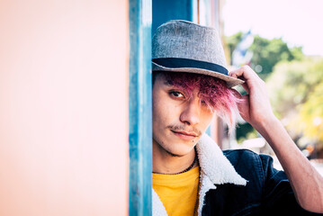 One young guy sitting outdoor with city buildings in background looking on camera with trendy hair and clothes. Leisure activity. Modern teen male posing outside and smiling confident